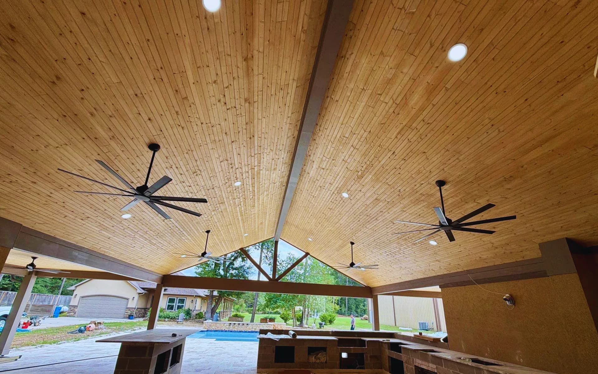 Vaulted tongue-and-groove wood ceiling with black ceiling fans and recessed lights over a covered patio